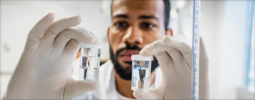 Man in a lab setting visually comparing two fluid samples in vials
