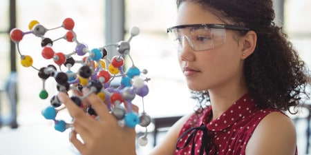A young person wearing eye protectors examining a molecular model