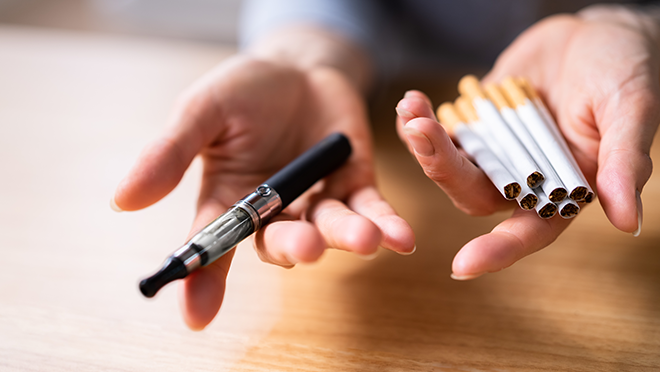 Open palms with cigarettes in one hand and an e-cigarette/vape stick in the other hand.
