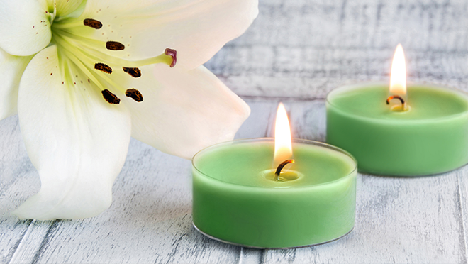 Two small green candles burning beside a white flower.
