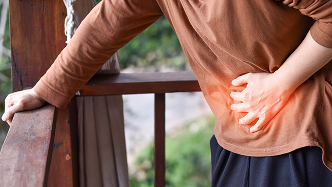 Person hunched over and holding a porch railing, clutching their stomach in pain.