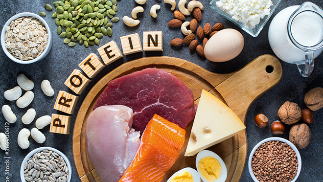 Raw meat, cheese, and boiled egg on a cutting board with the word protein, an array of nuts, beans, and seeds, and milk.