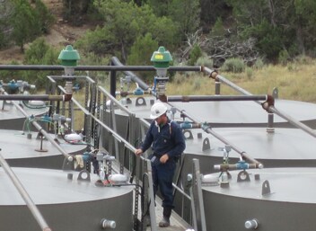 Worker preparing to gauge oil production tanks.
