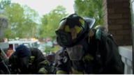 Shows a firefighter in full gear at a row house fire.