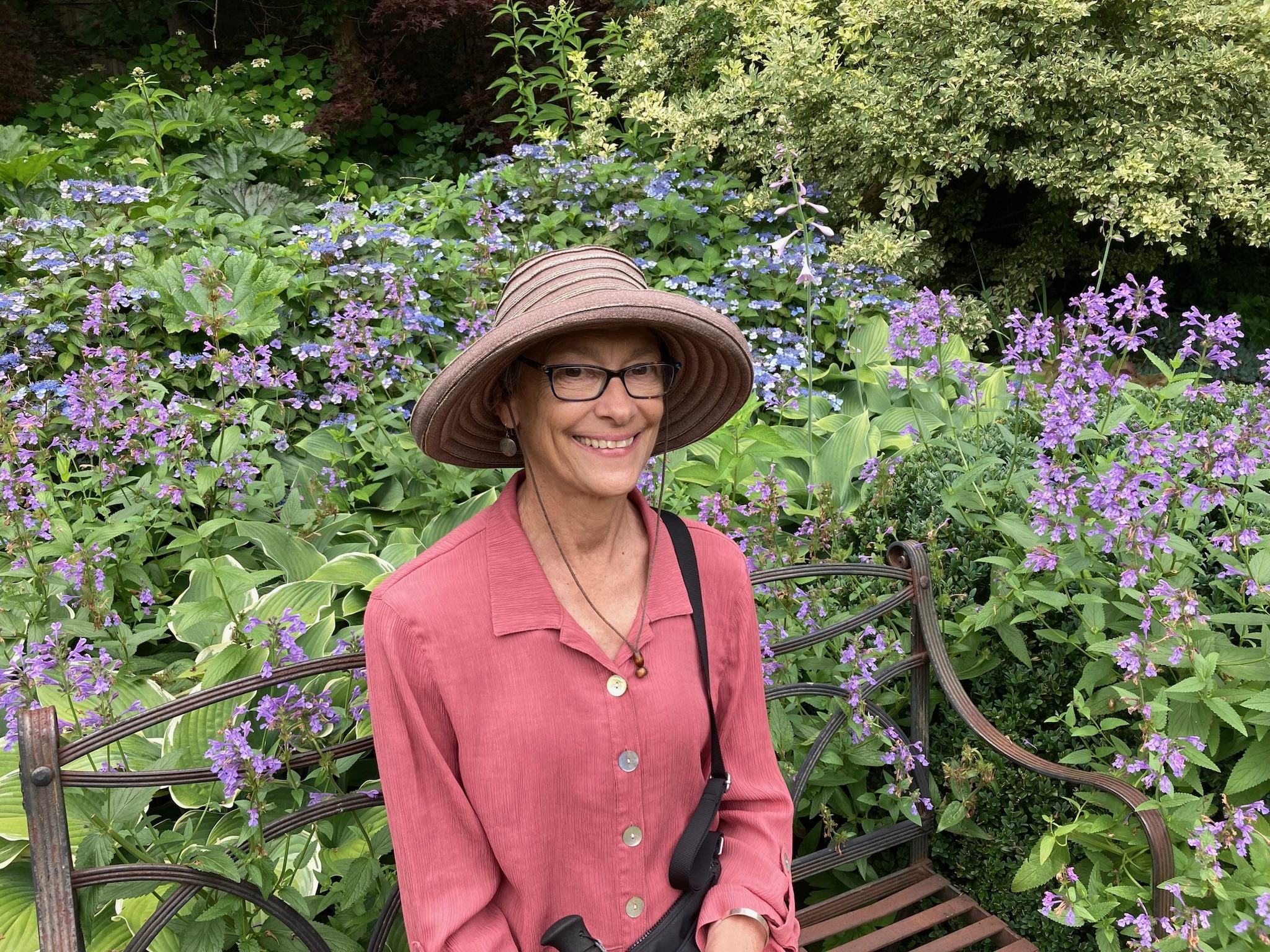 Photo of Jessica Kogel standing in front of purple wild flowers. She is smiling and wearing a pink short and large hat.