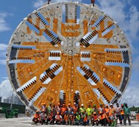 Approximately twenty workers posing in two rows in front of a very large Working Face of a Tunnel Boring Machine (TBM)