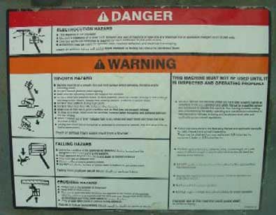 The warning label on the aerial platform illustrates the hazards of electrocution, falling, or striking an overhead obstacle.