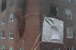 Tarps over a window and smoke rolling from another window.