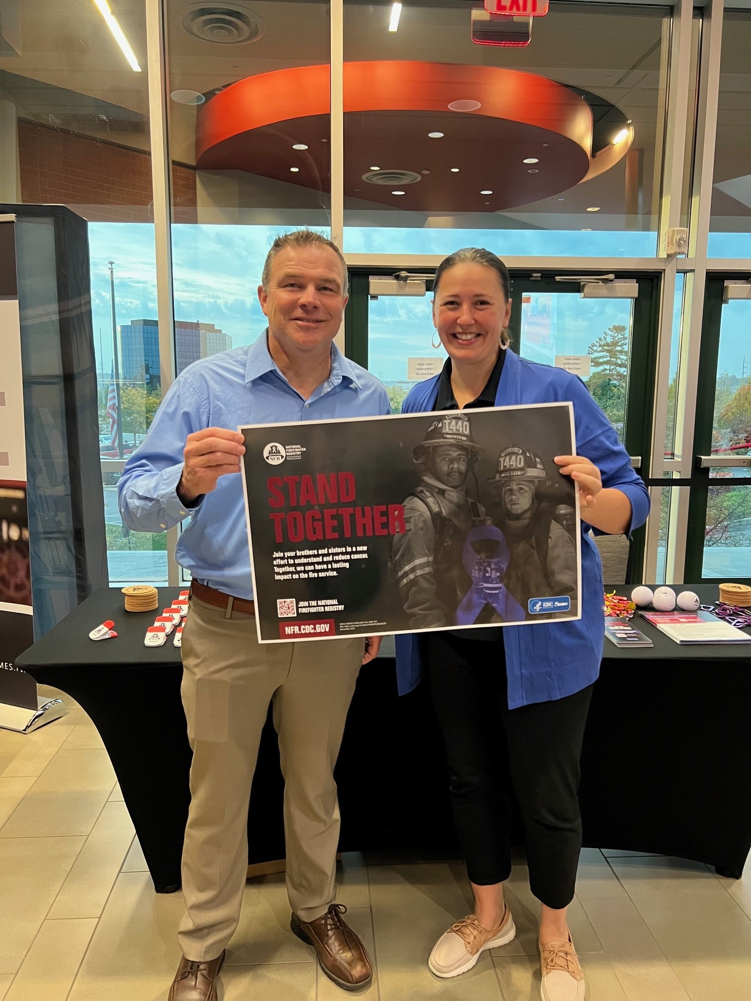 Two people at a conference booth holding up a poster promoting the NFR that says stand together in bold red letters.