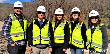 Four NIOSH investigators and one resident rotator take a group photo while wearing hard hats and reflective vests during a site visit in Utah