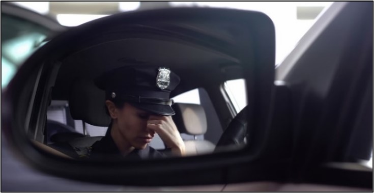 Photo of police officer reflected in a vehicle side mirror looking distressed.