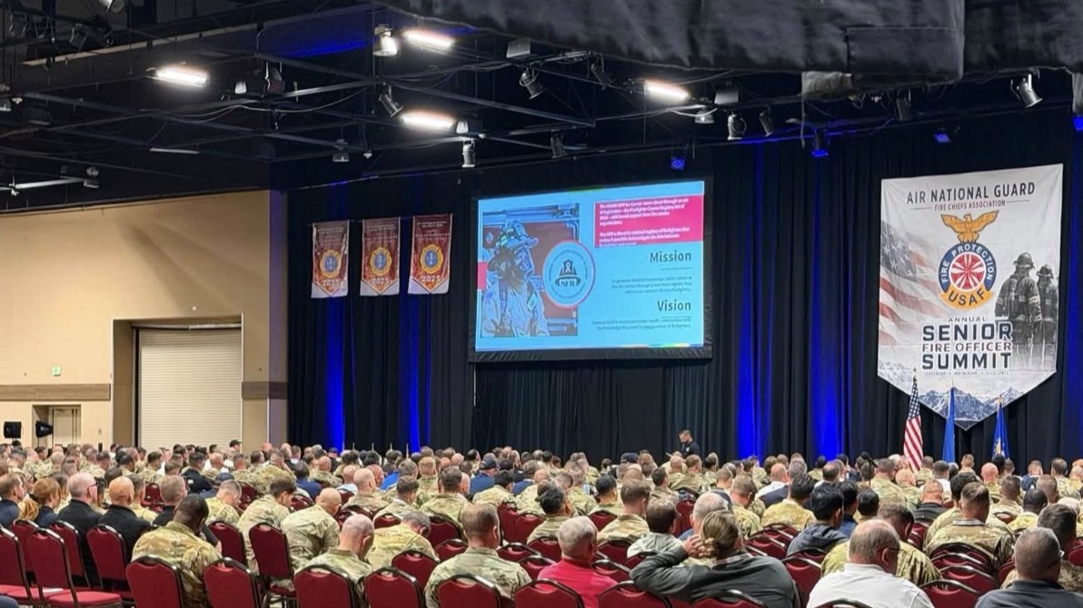 Man on stage, presenting to large group of military members.