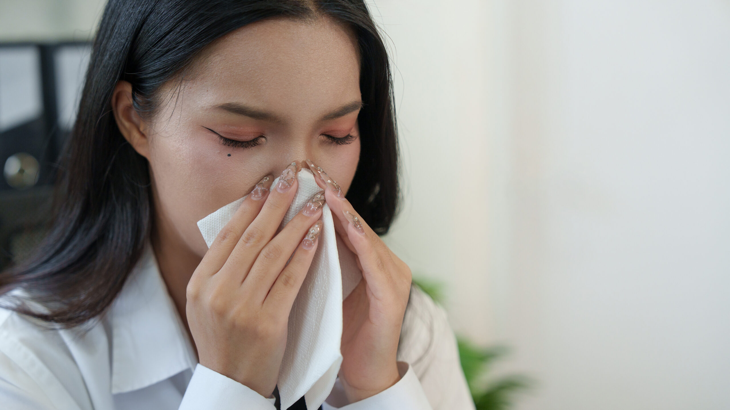 A female with her eyes closed holding a tissue to her nose.