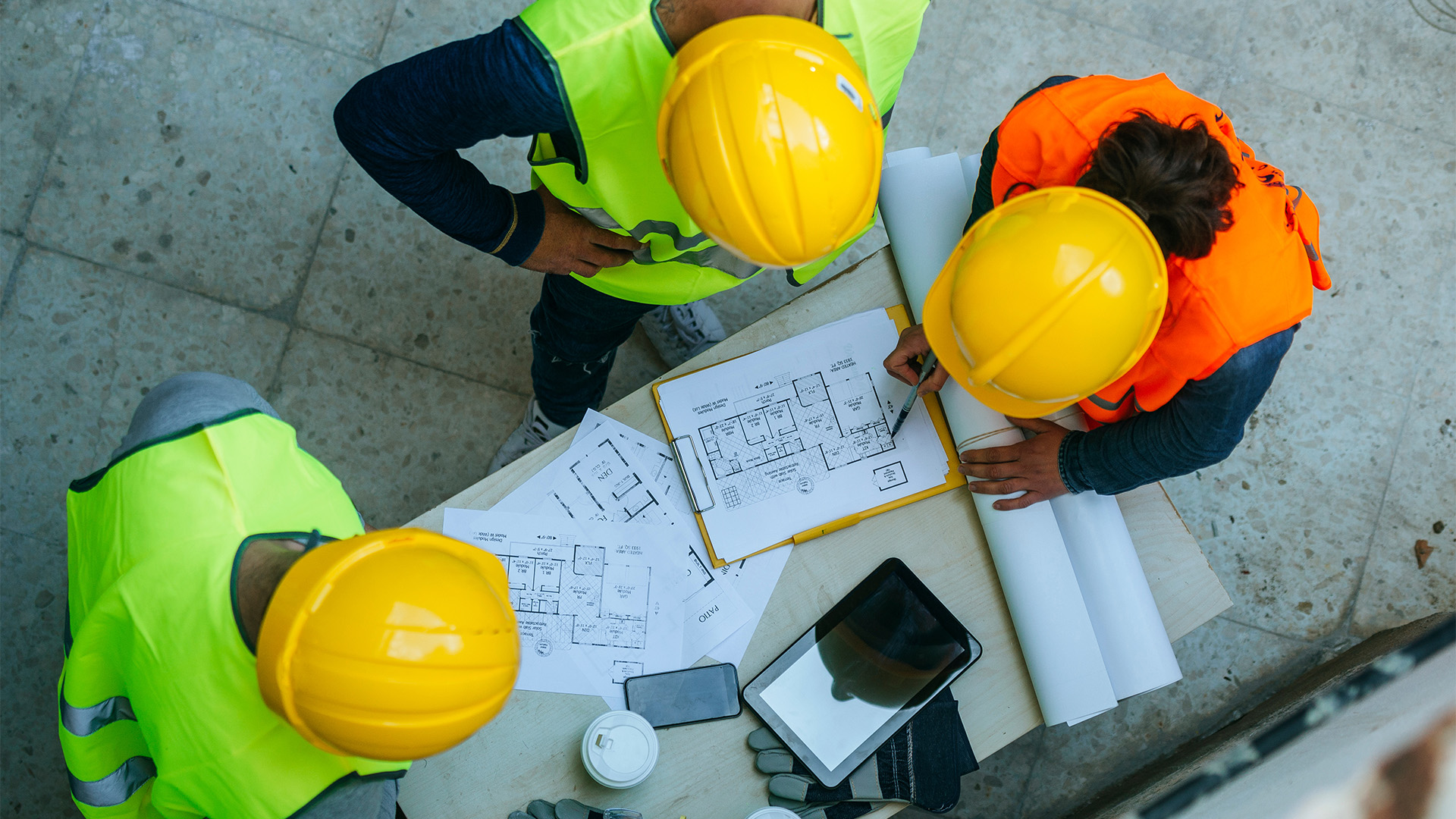Three workers in hard hats looking over plans.