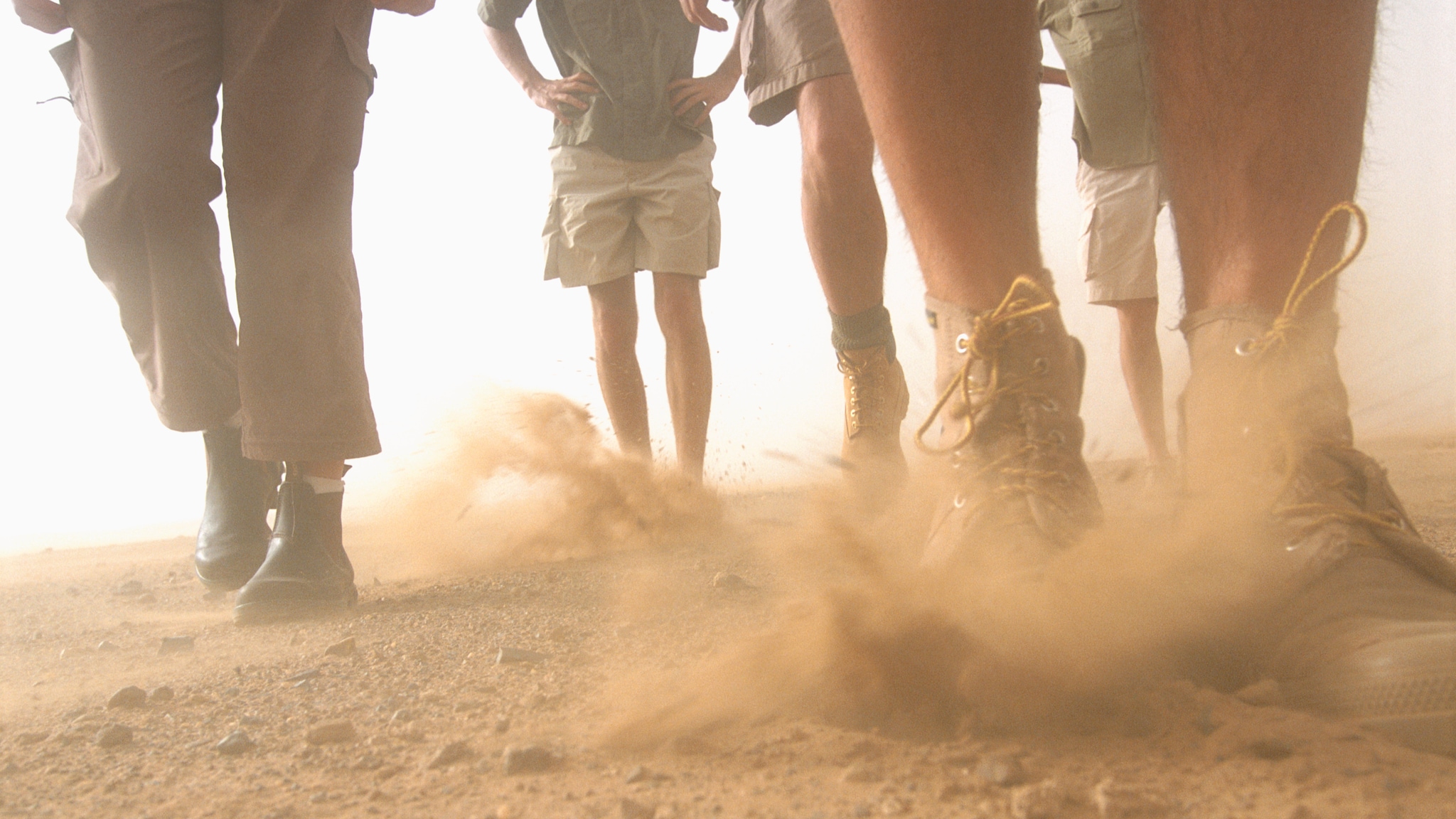 Photo of people's legs walking on dusty soil.