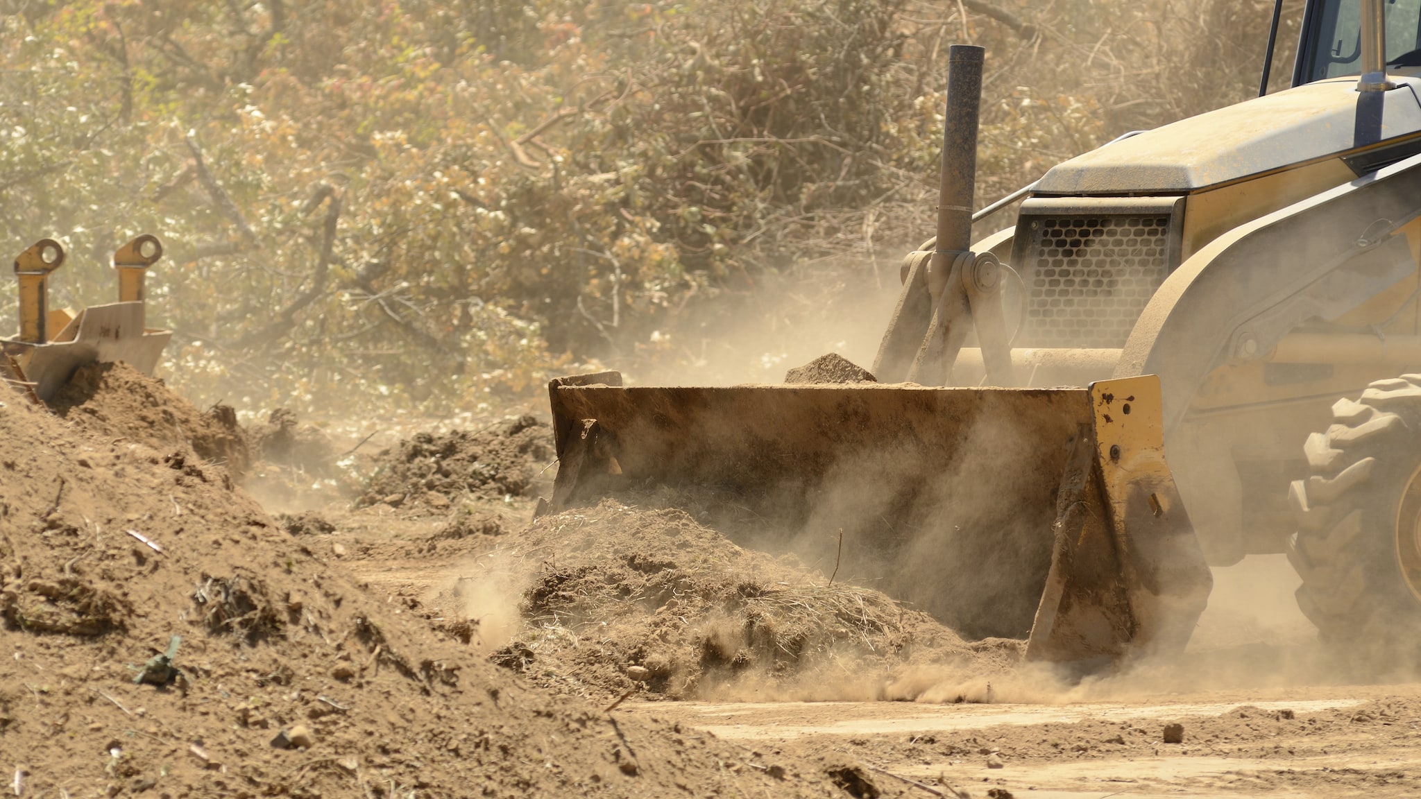 Bulldozer pushing dirt with dust.