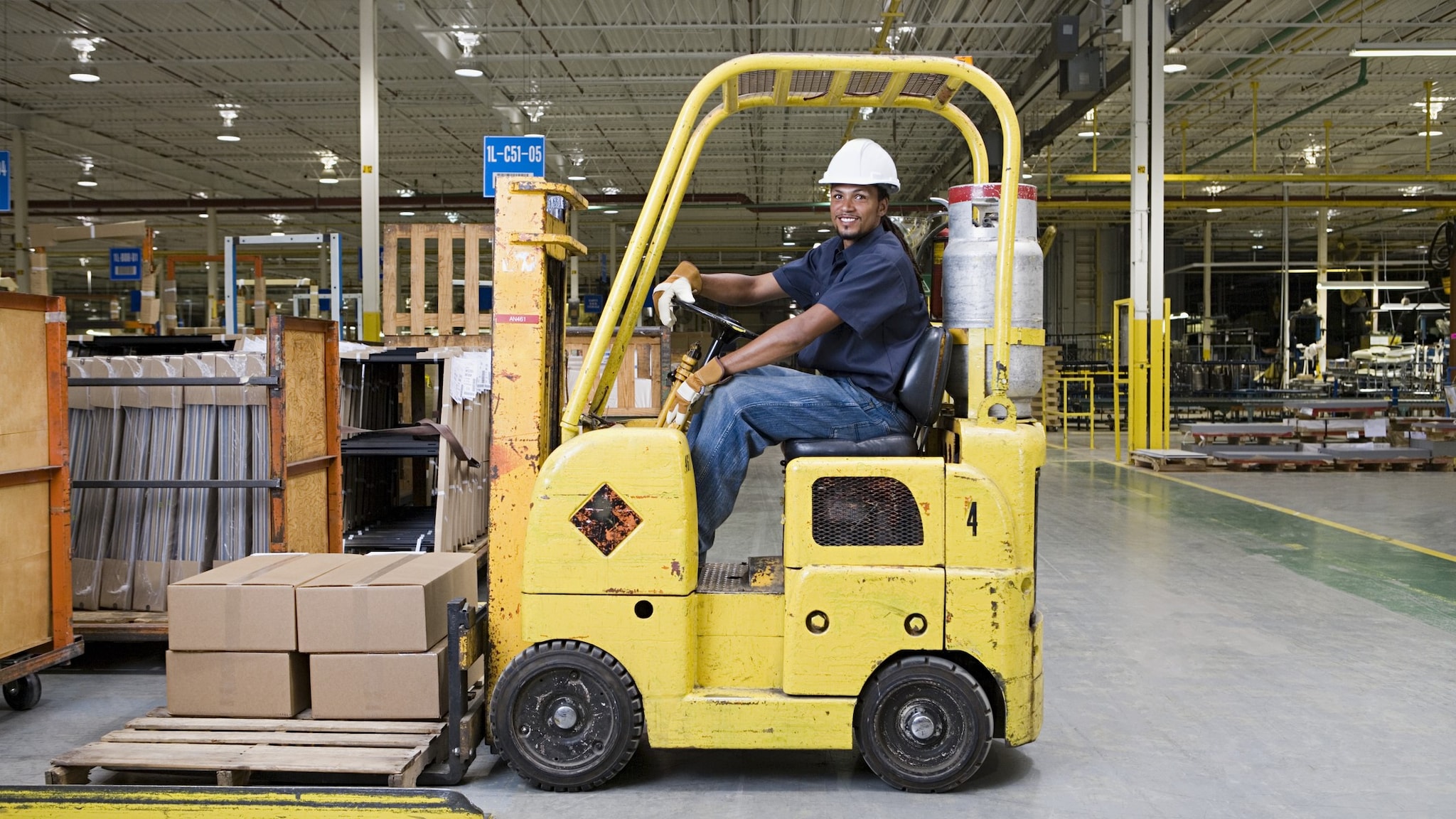 A man sits in a forklift in a well-lit warehouse.