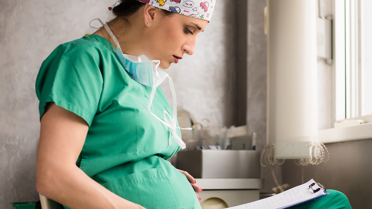 Pregnant healthcare worker reading a chart on a clipboard.