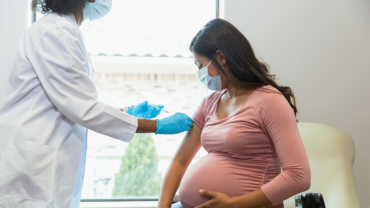 Female healthcare provider working with a pregnant patient, both wearing PPE.