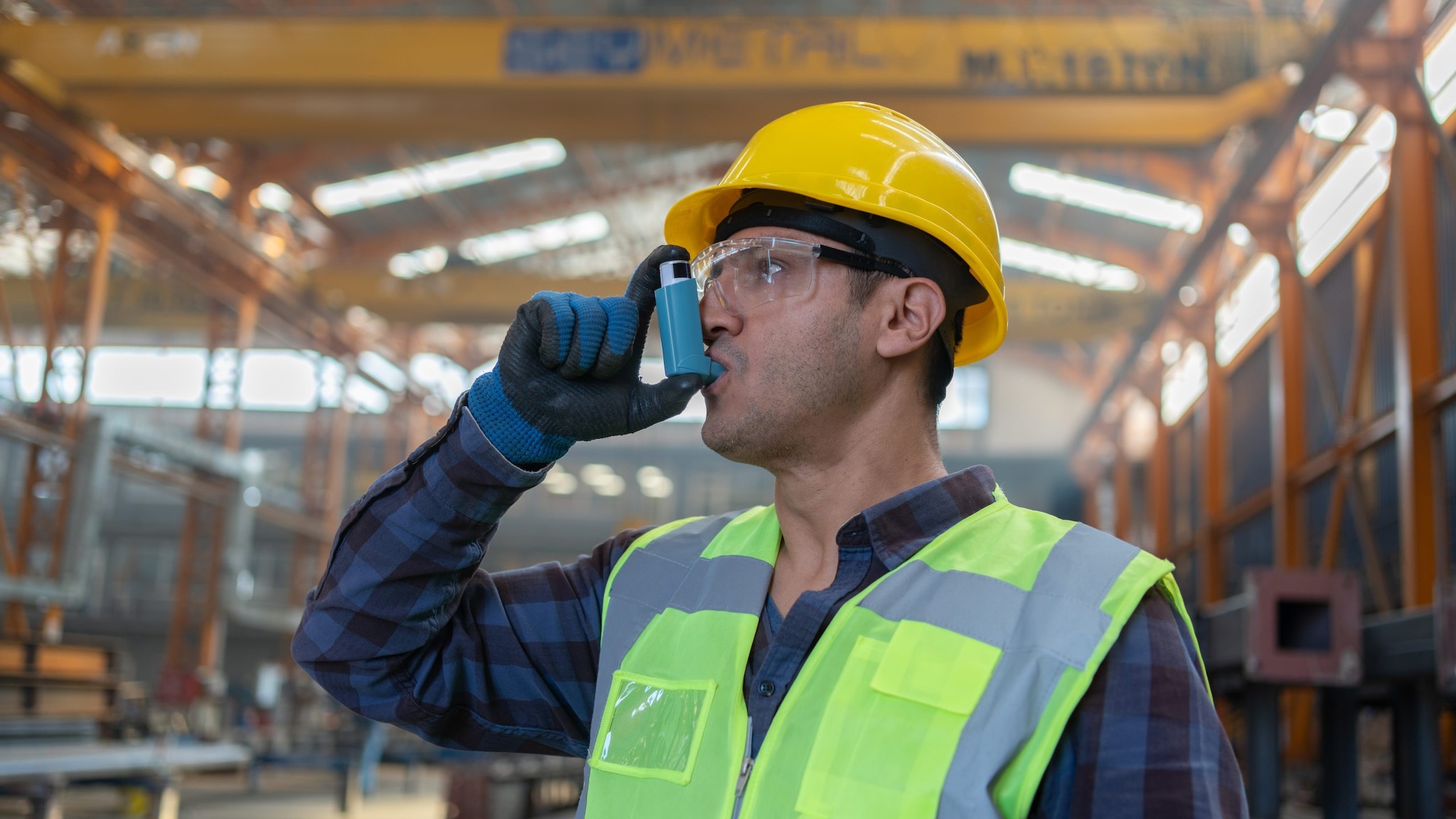 Man at work, wearing a hard hat and using an inhaler. Image by Getty Images.