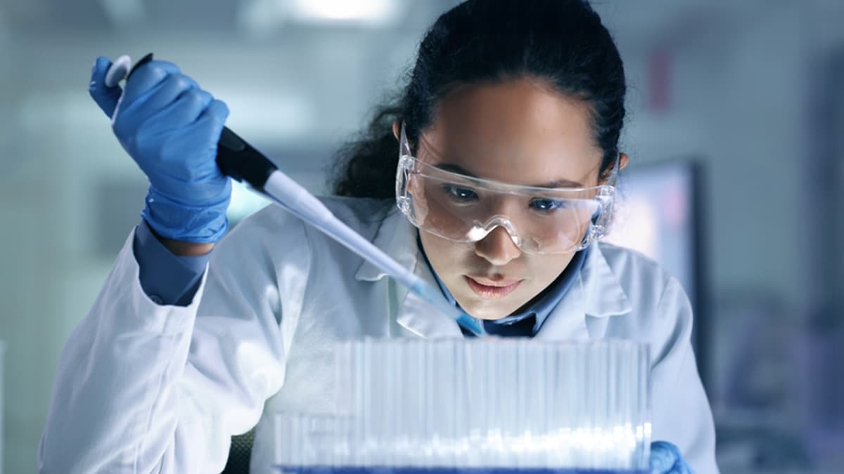 Female scientist analyzing medical sample in test tube. Young researcher is wearing a white lab coat.
