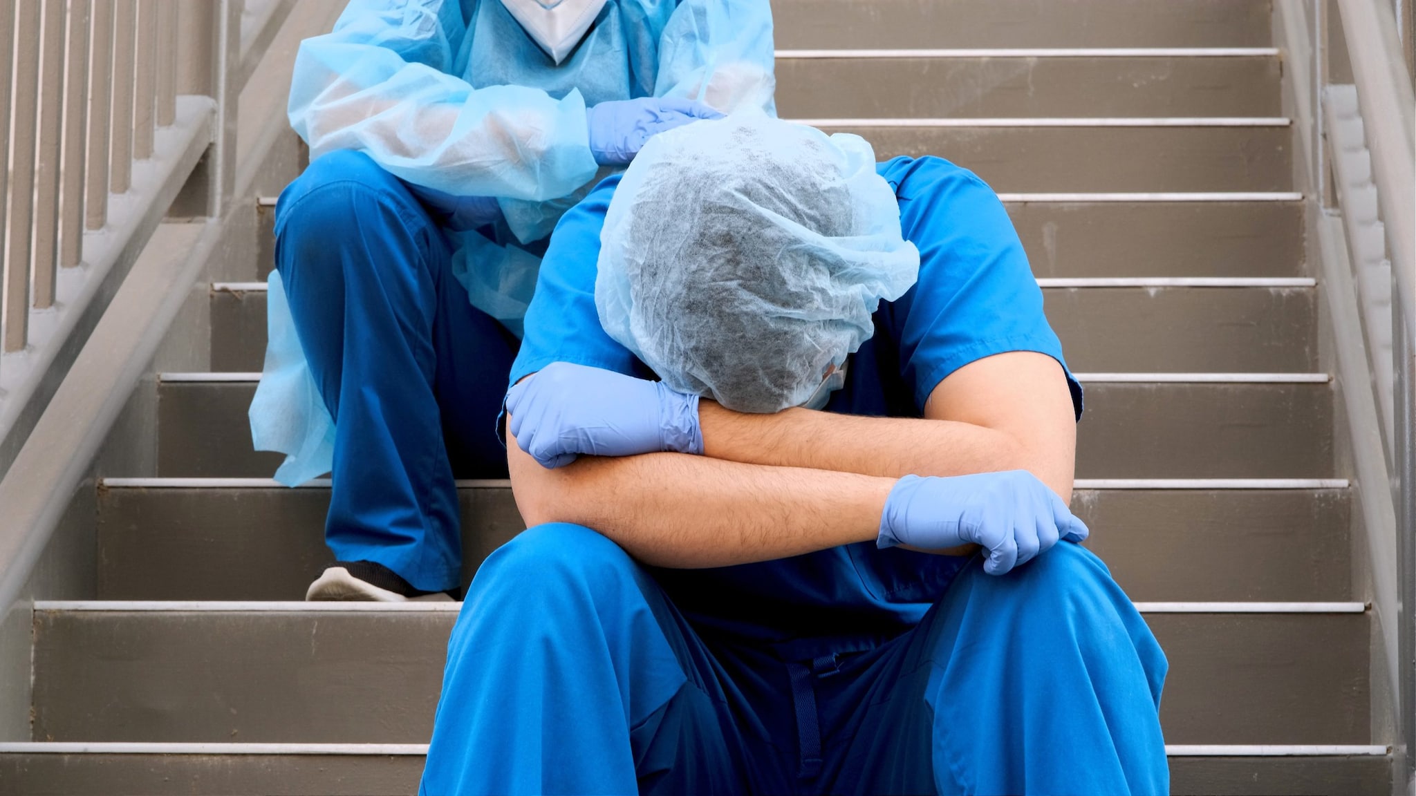 Two overworked healthcare workers sitting on stairs.