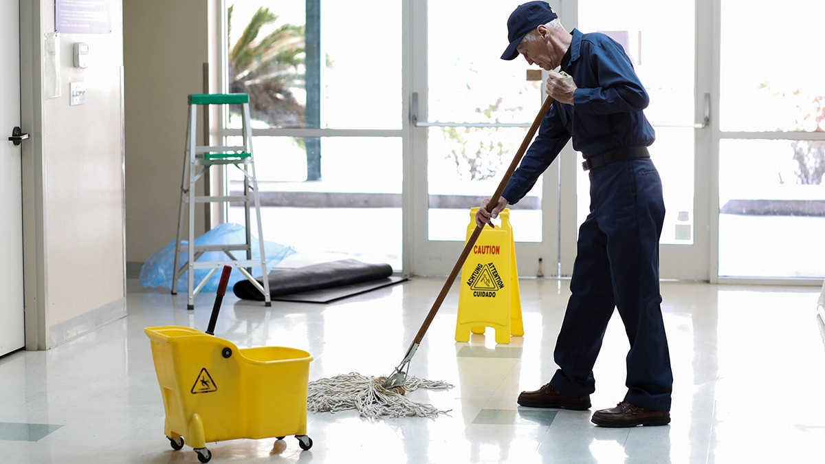 Senior adult janitor mops floors at entry to offices.