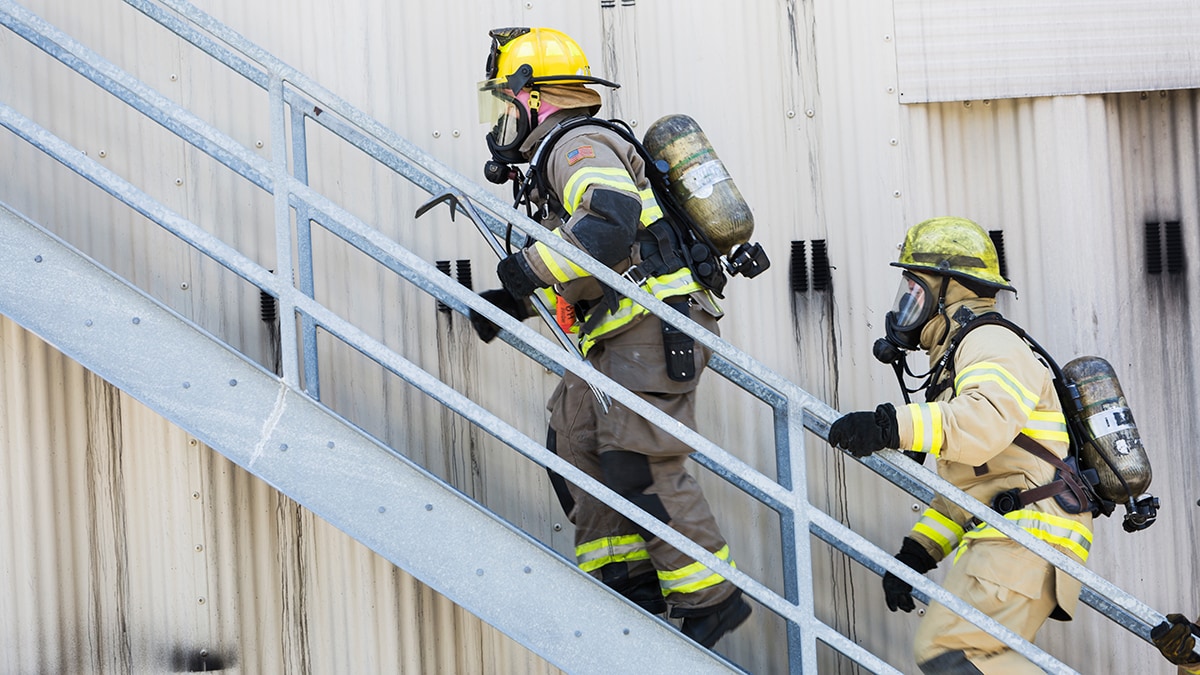 Two firefighters in gear climb exterior stairs
