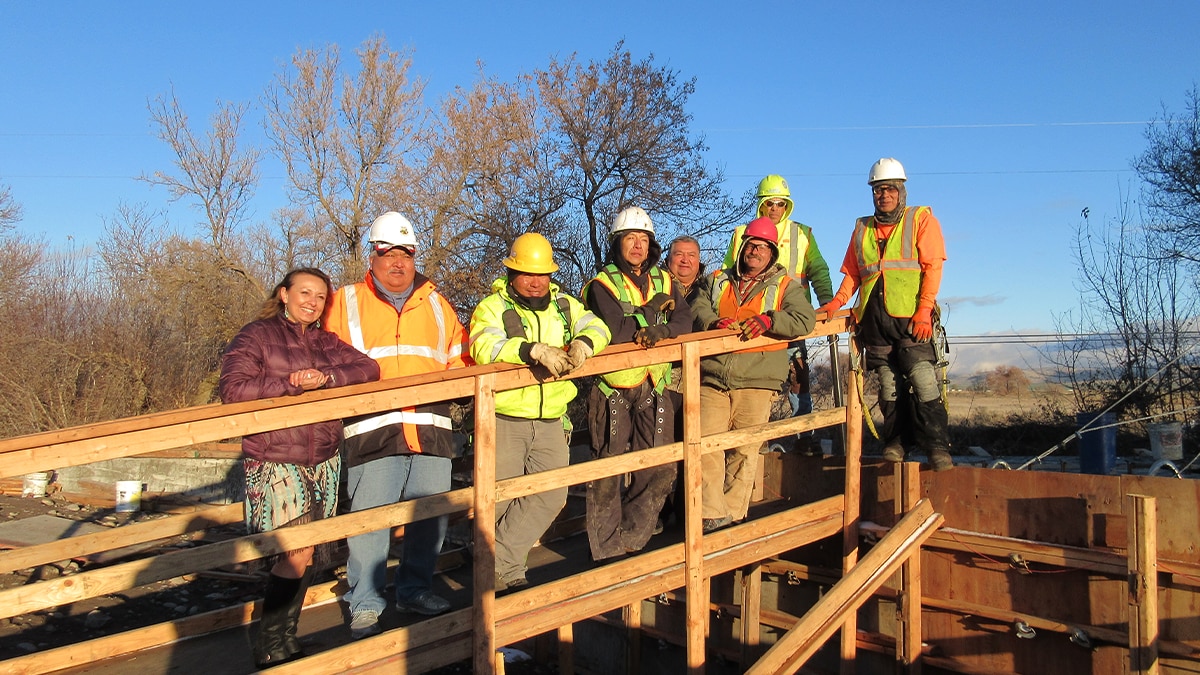 Male American Indian/Alaska Native construction workers standing on a bridge facing the camera.