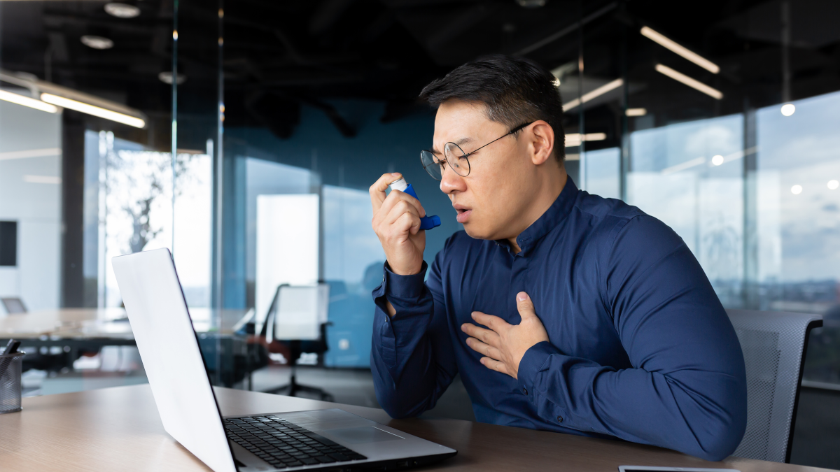 Worker using inhaler working on his laptop.