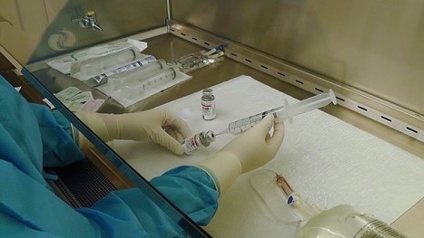 Person wearing a gown and gloves preparing a syringe under a fume hood.