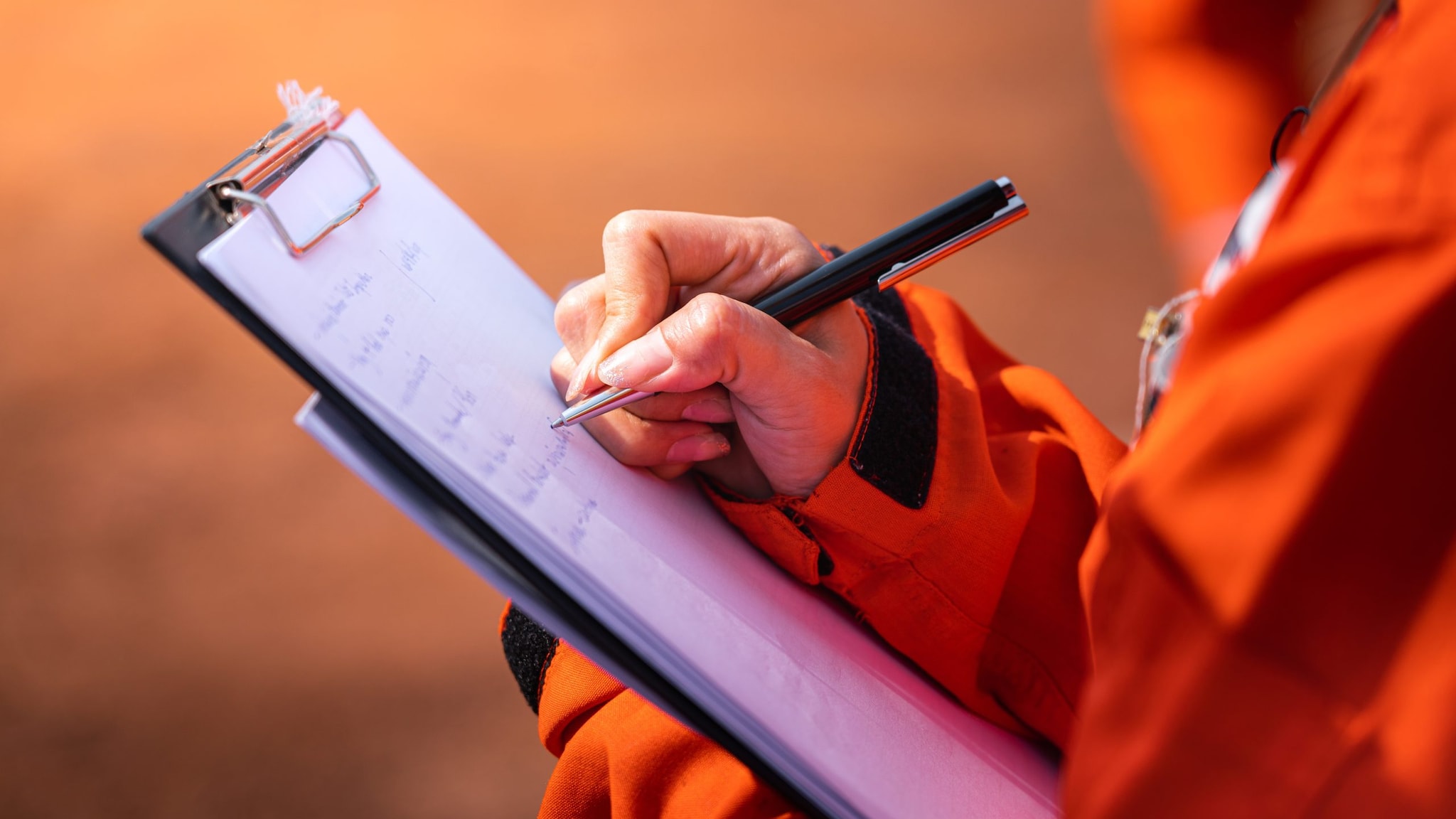 Person in a safety jacket writing note on checklist paper during an audit.