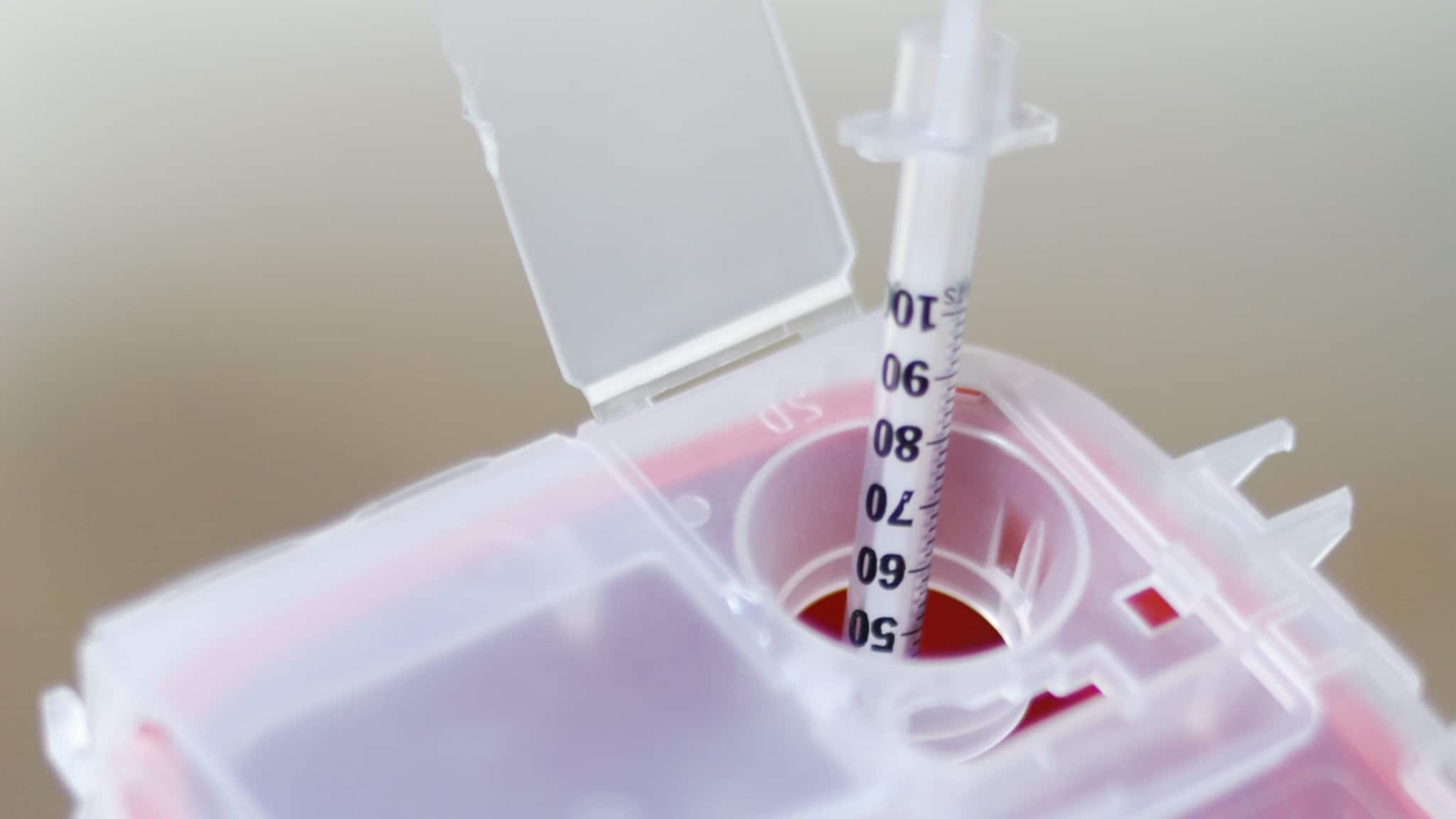 A needle being placed in a sharps disposal container.