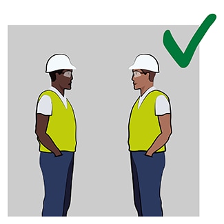 Illustration of two workers standing in an open area and communicating comfortably, with a green check mark in the corner of the image used to represent this activity as a good practice in relation to communicating on a job site away from noise.