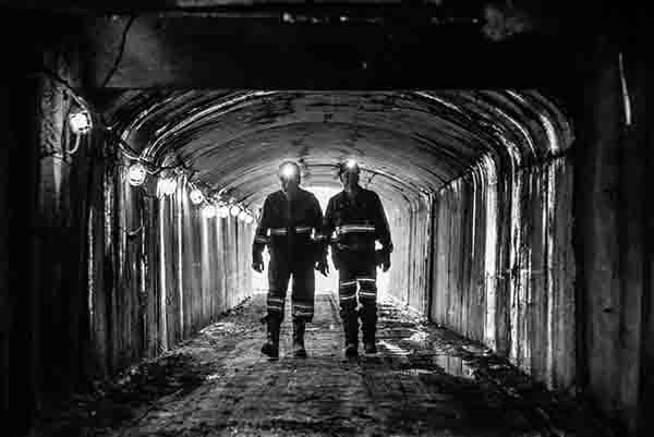 Two miners are backlit as they walk into an underground mine.