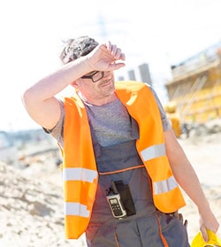 Man in reflective worker vest wiping sweat off his brow.