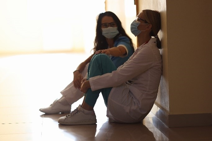 Two female health workers wearing masks and sitting on the floor