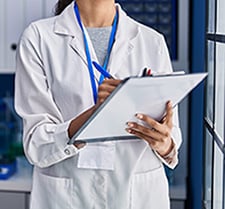 Person in white lab coat writing on clipboard