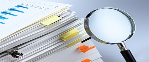 Stack of papers with a magnifying glass suggesting investigation and analysis