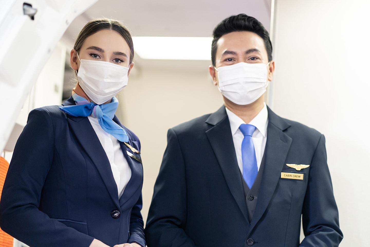 Asian flight attendants wearing face mask waiting for greeting passengers coming on board in airplane during the Covid pandemic to prevent coronavirus infection. Healthcare in transportation concept.