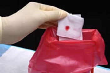gloved hand holding Bloody-stained gases over disposal bag