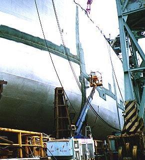 Workers using powered manlift along the side of a ship.
