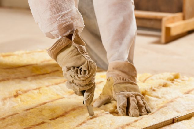 Worker cutting fibrous glass insulation material.