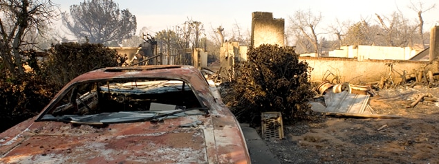 Burned remains of vehicle and house after wildfire in California.