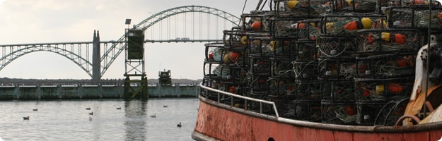 An image with a Dungeness crab vessel loaded with pots in the foreground and the Yaquina Bay Bridge in the background. Photo by NIOSH