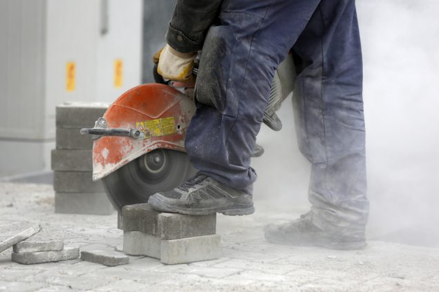 A worker cutting brick pavers using a masonry saw. 