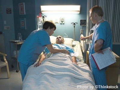 Two medical staff in a hospital room attend a patient in bed