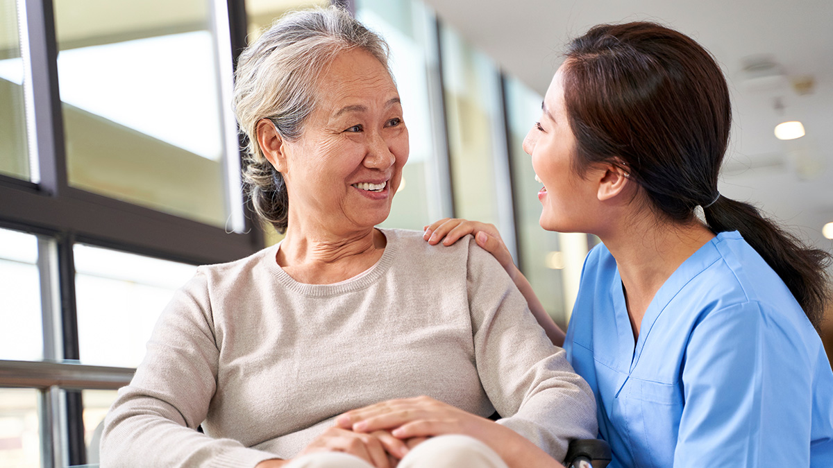 Friendly caregiver talking to senior woman in hallway of nursing home