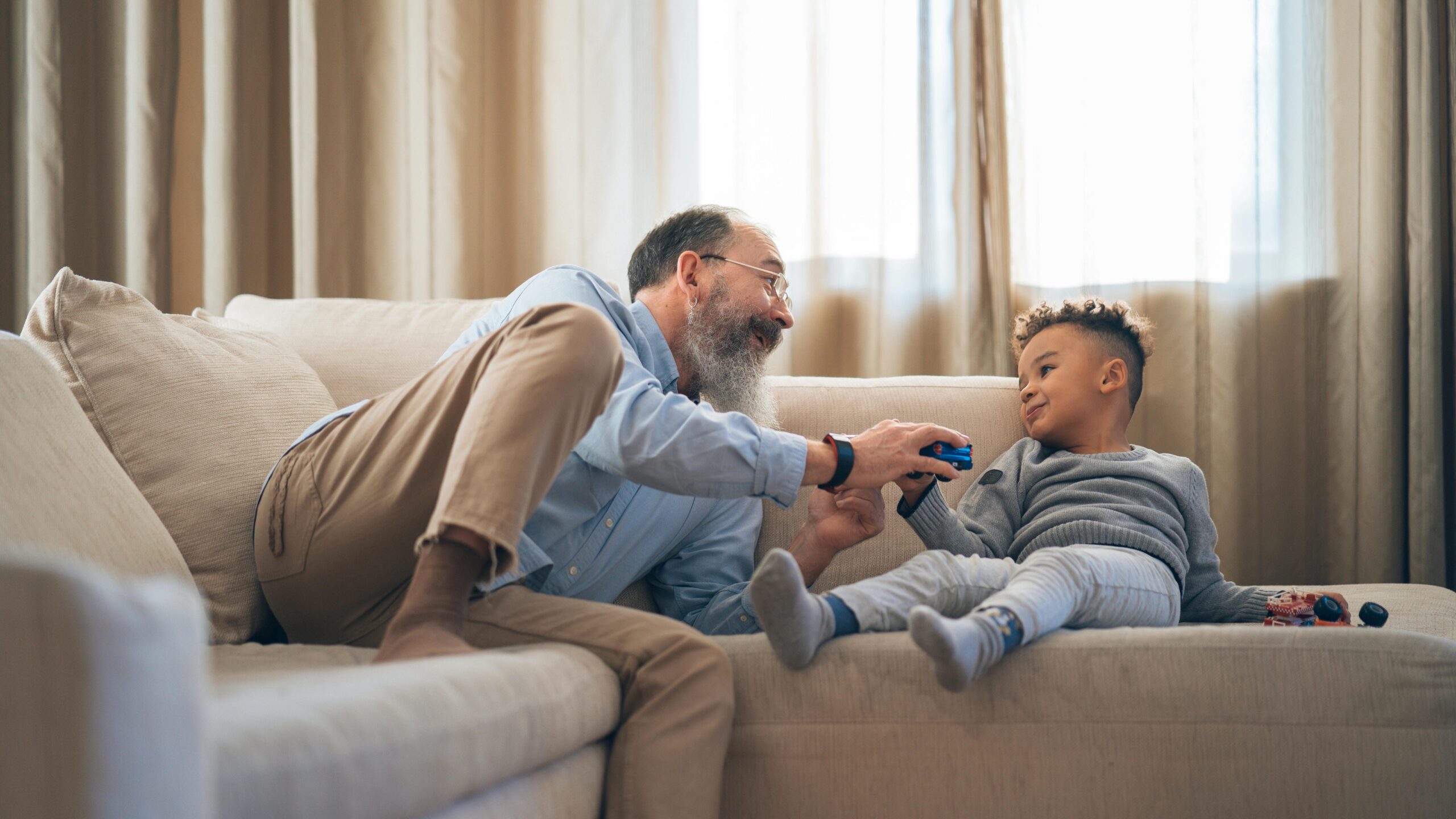 A heartwarming moment between grandfather and grandson laughing and playing on a cozy sofa indoors