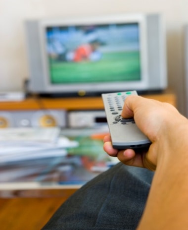 Man at home with remote in his hand watching a soccer game on television.